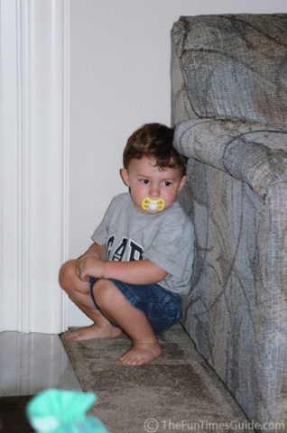 A diaper-wearing toddler 'doing his business' -- he thinks he's hidden behind the sofa and the wall!